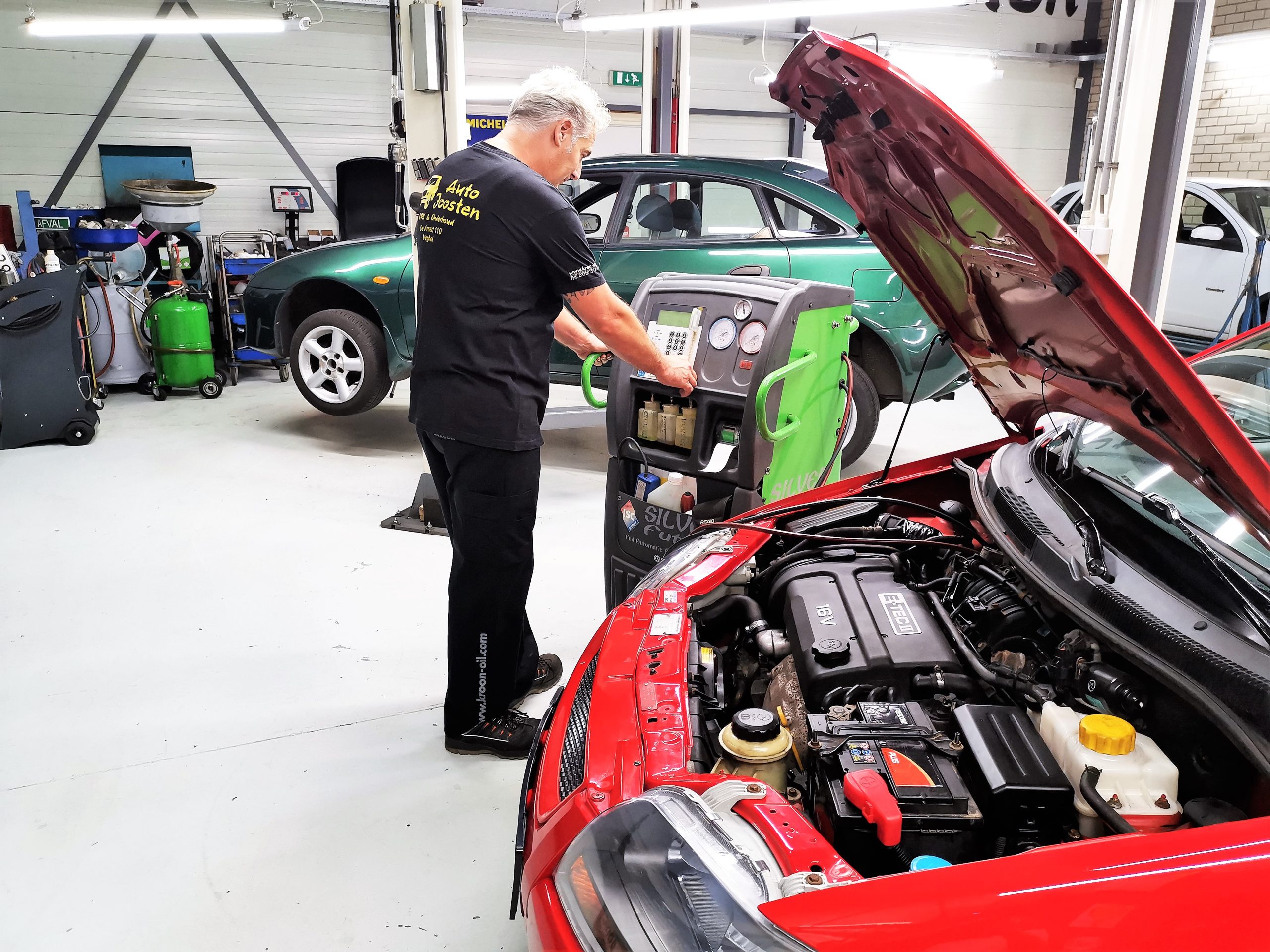 Monteur werkt met het airco-apparaat aan een rode Opel met open motorkap
