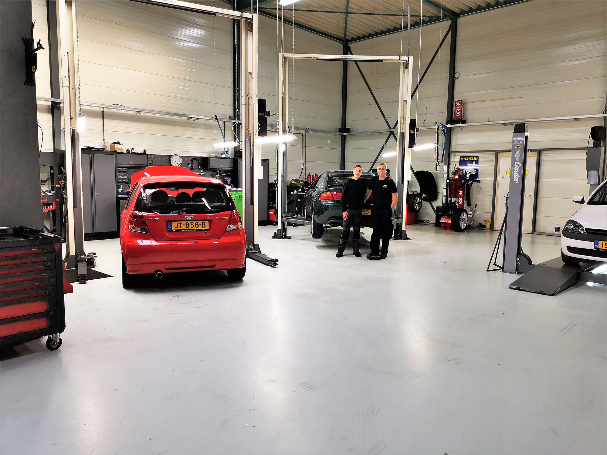 Overzicht van de werkplaats met twee monteurs en een rode Toyota