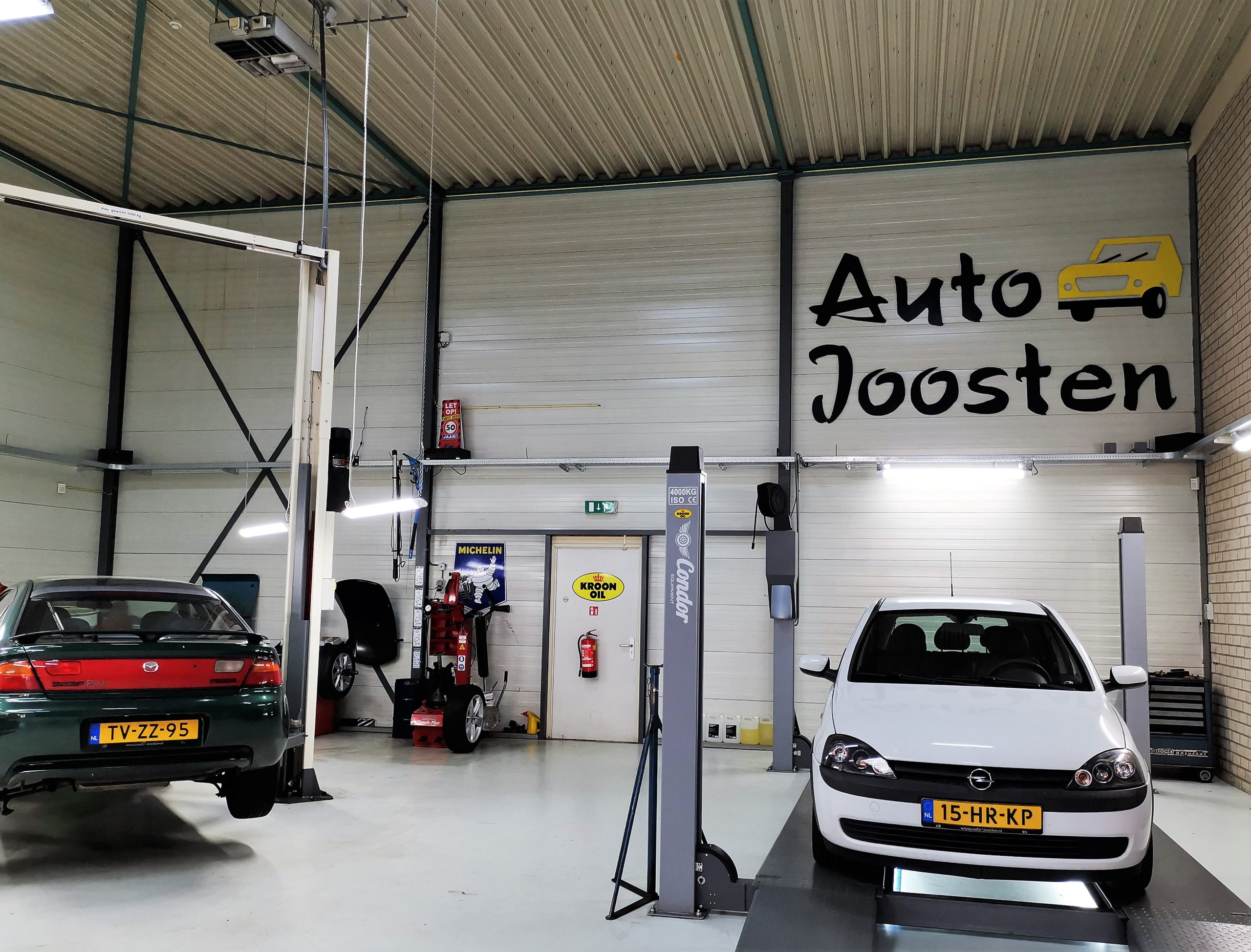 De werkplaats van Auto Joosten in Veghel met de naam op de muur, een Mazda en een Opel Corsa op de brug
